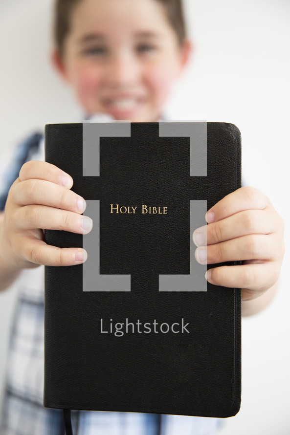 a boy child holding out a Bible 