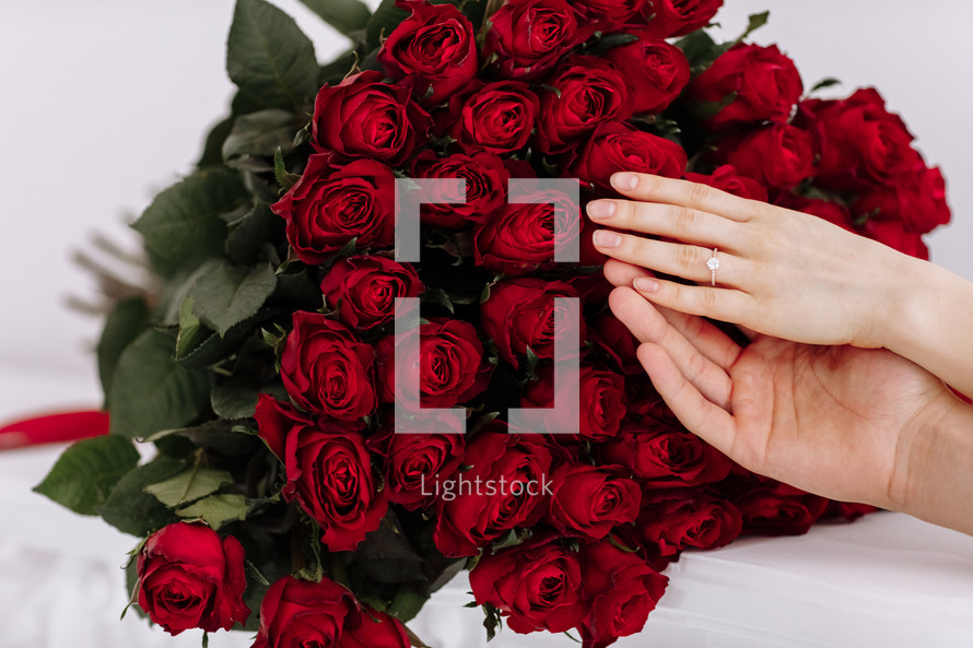 close-up of man and woman hands with engagement rings. Hands of the on the background of the big bouquet of red roses. romantic proposal time.