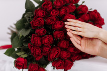 close-up of man and woman hands with engagement rings. Hands of the on the background of the big bouquet of red roses. romantic proposal time.