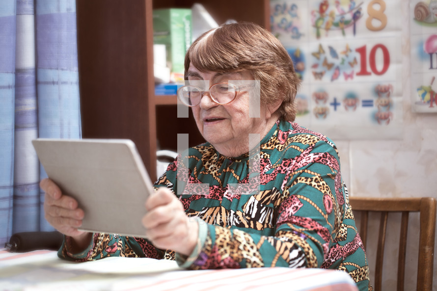 Elderly woman in glasses watching something on pad