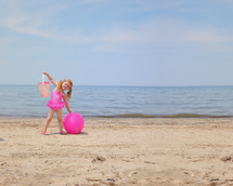 a little girl on a beach with a sand bucket and ball 