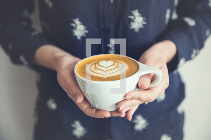 woman holding a cappuccino with a heart design.