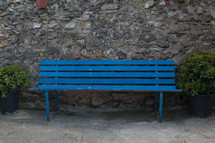 An empty blue bench against a rock wall.