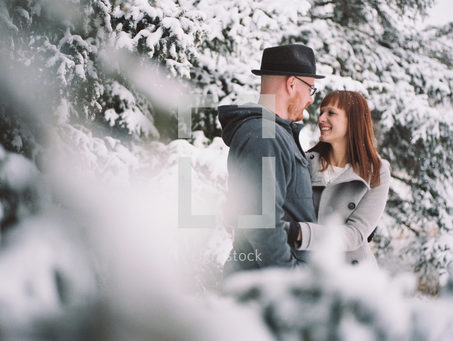 a couple in winter coats hugging outdoors in the snow 