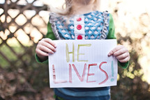 girl child holding a sign that says "He Lives!"
