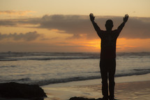 silhouette of a man with raised arms standing on a beach at sunset 