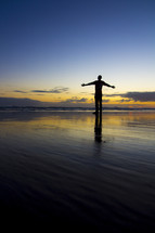 man with open arms at a beach at sunset 
