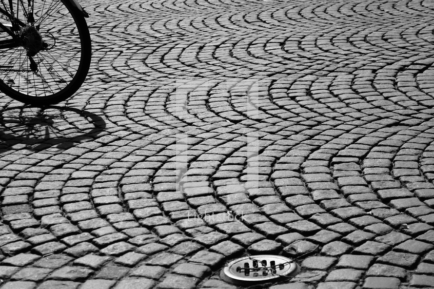Bicycle wheel on arched cobblestone street.