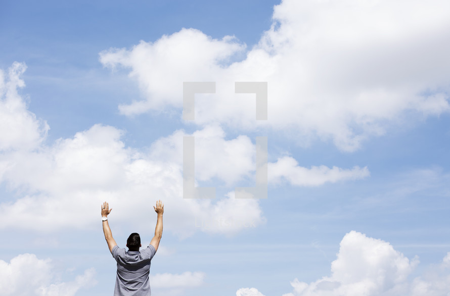 man with raised arms standing outdoors with blue skies as background 