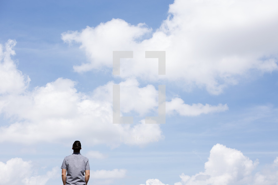 man with his back to the camera looking up with blue skies in background 