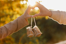 Man and pregnant wife are doing heart gesture with hands and holding warm baby shoes on nature autumn background. Future parents waiting for the baby. The concept of Mother's Day and Women's Day