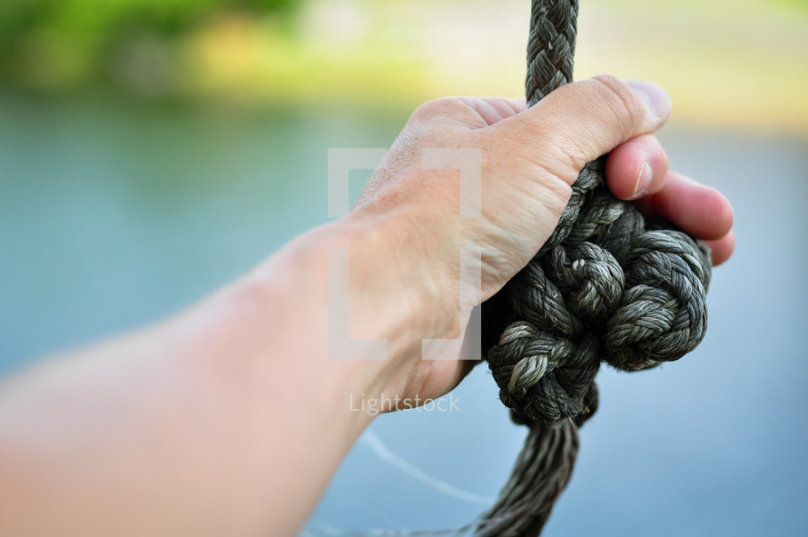 Mans hand grasping a knotted rope