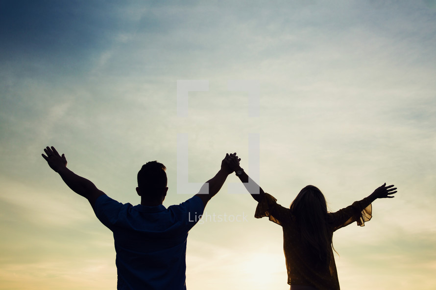 silhouette of a couple standing with raised hands 