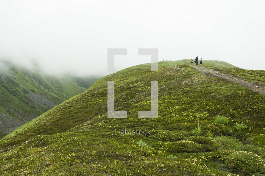 people hiking on a green mountaintop 