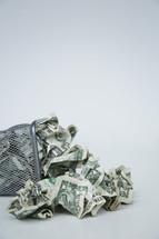 crumpled dollar bills in a trash can 