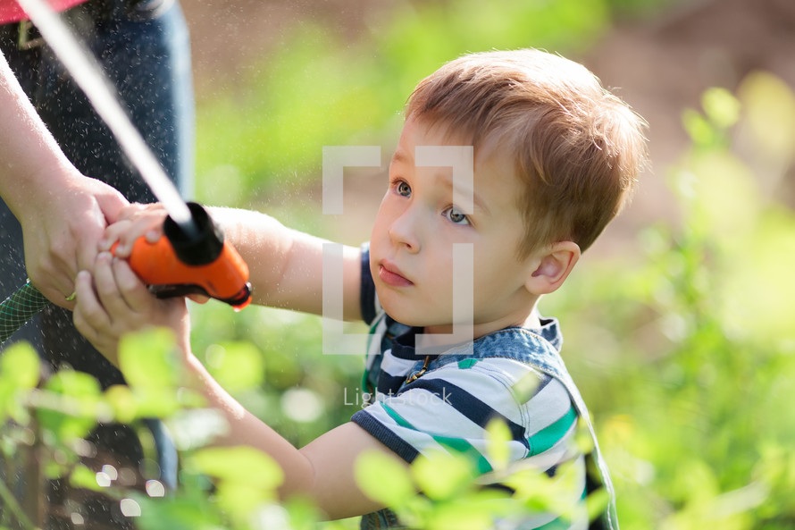 a boy holding a watering hose in a garden 