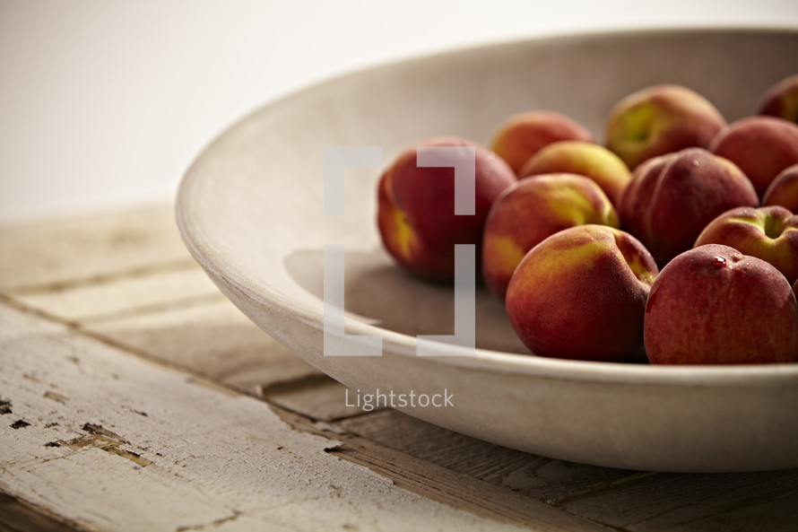 Peaches in a bowl sitting on a wooden table