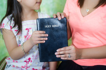 Mother handing Bible to her daughter.