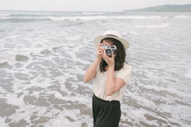 a woman holding a camera standing on a beach 