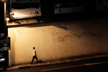 a man walking down a city sidewalk alone at night 