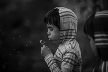 a boy blowing on a dandelion outdoors 