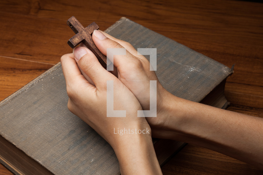 holding a prayer cross over a Bible and praying 
