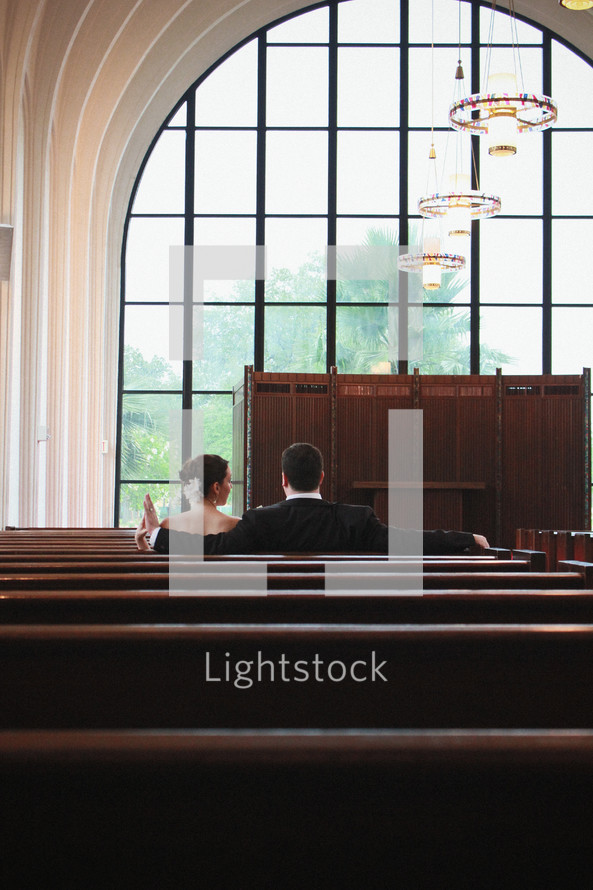 bride and groom sitting in church pews