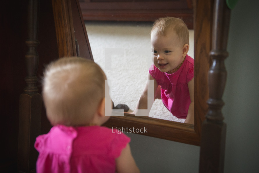 A baby girl looks at herself in the mirror.