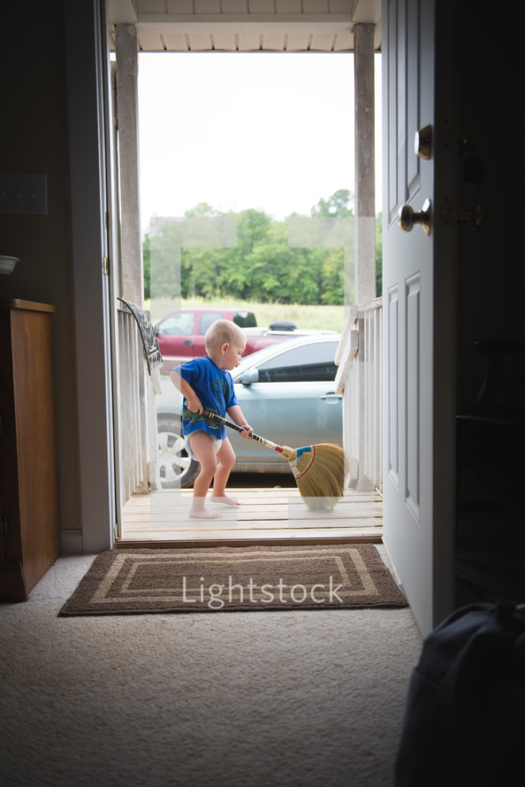 A toddler sweeping the porch.