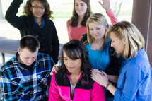 teens with their hands on a friend in prayer