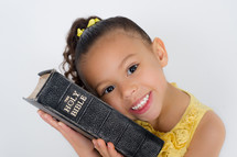 Little girl holding a Bible against her cheek.