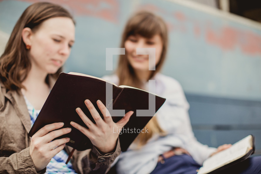 women reading Bibles while sitting on a park bench