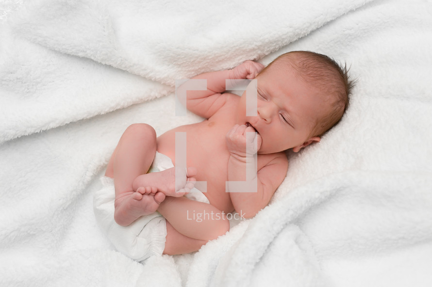 newborn in a diaper lying on a white blanket