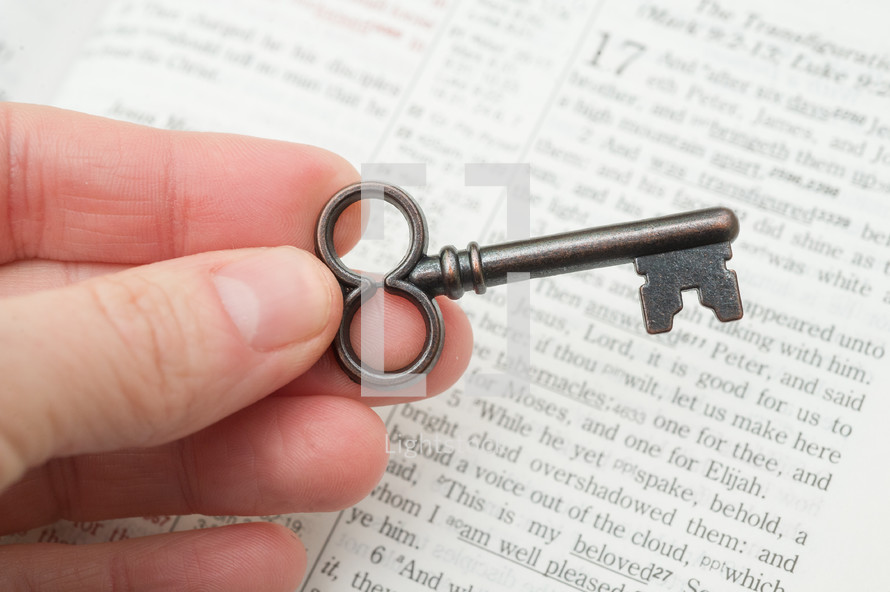 hand holding a key over the pages of a Bible