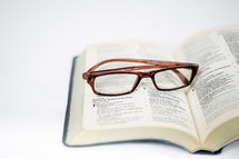 An open bible with a pair of glasses laying on it