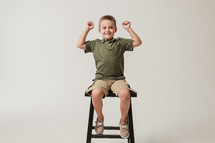 boy child sitting on a stool showing his muscles