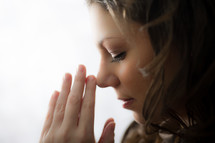 a young woman with her hands held in prayer to God