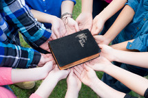 all hands supporting a Bible