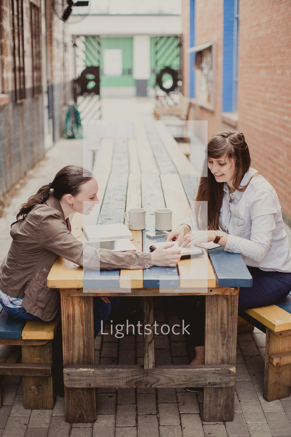women discussing the Bible while sitting at a picnic table outdoors 