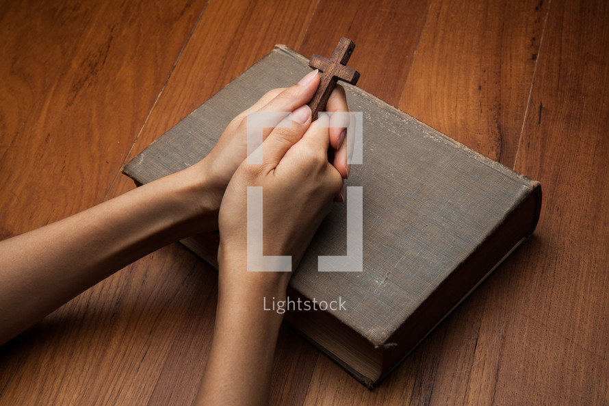 holding a prayer cross over a Bible and praying 
