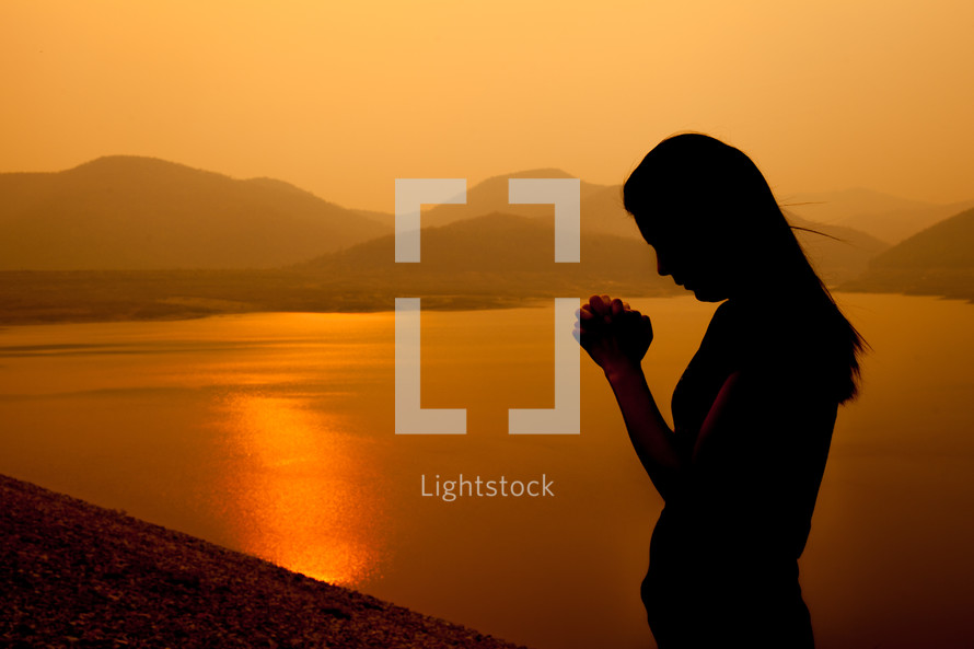 a woman praying by a lake at sunset 