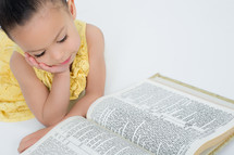 Little girl with her face propped up in her hands, looking at an open bible
