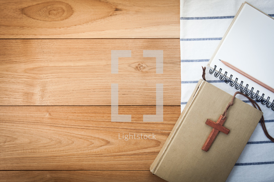 notepad, pencil, cross on a lanyard, and Bible on a wood table 
