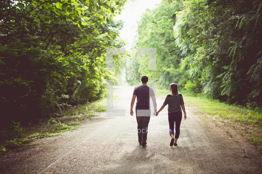 a couple walking holding hands on a dirt road 