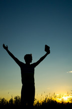silhouette of a man with raised hands holding a Bible 