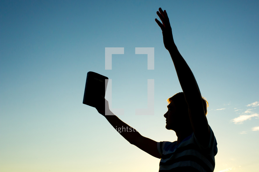 silhouette of a man with raised arms holding a Bible 