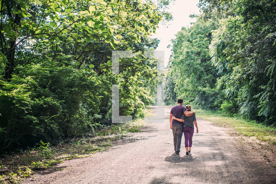 young couple embracing walking down a dirt road 
