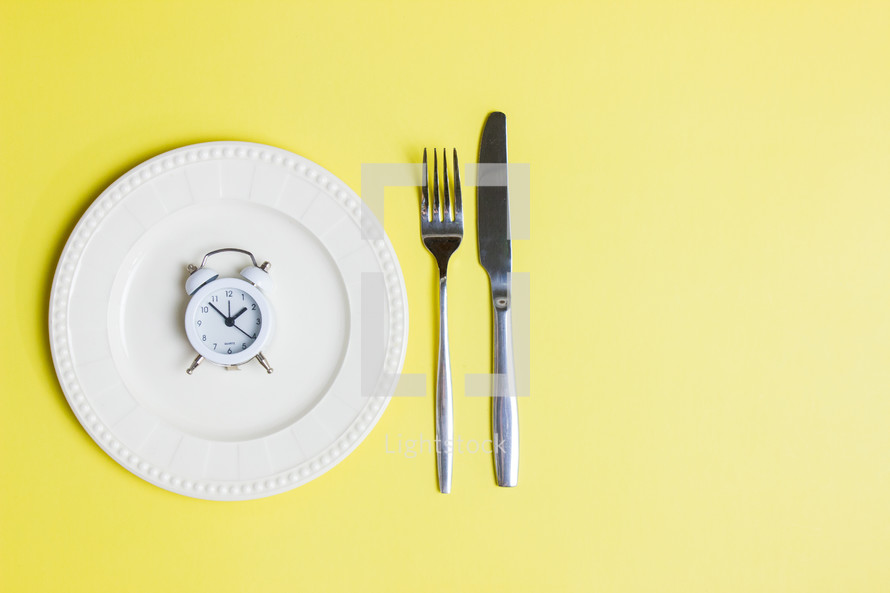 Diet concept with spoon and knife and clock over the yellow background. 