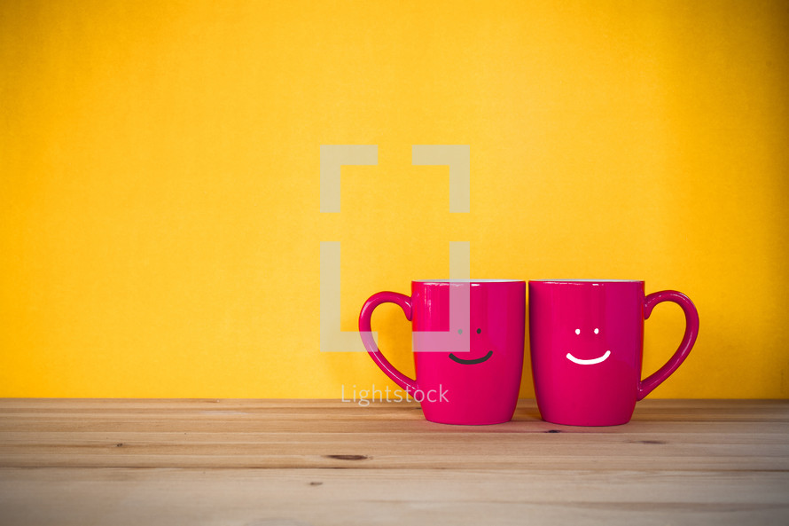two red mugs against a yellow wall 