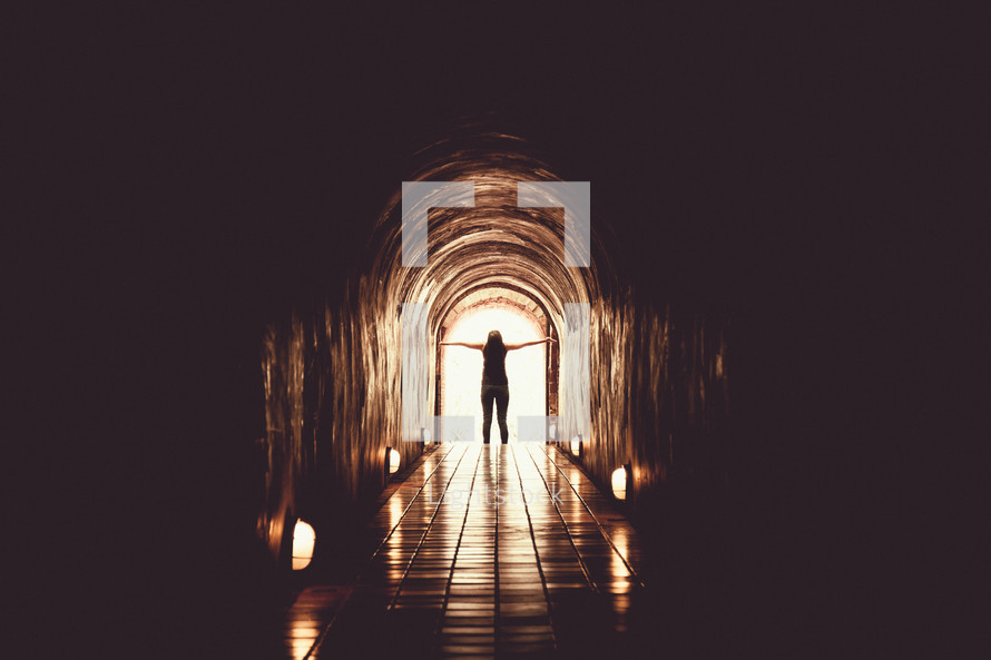 a woman standing at the end of a dark tunnel 